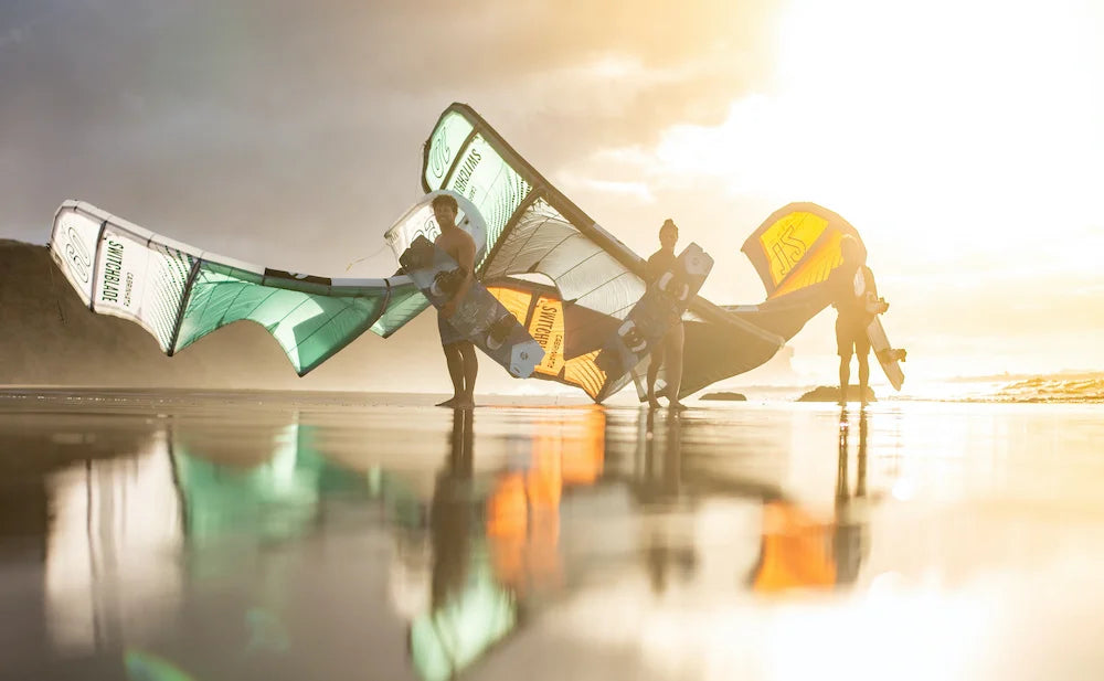 Drei Kitesurfer laufen in de Sonnenuntergang